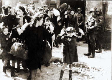 People being forced out of the bunkers and marching at gunpoint to the deportation area. This photo was taken as part of a German military report to glorify the destruction of the Warsaw Ghetto. The report was later used as evidence in the Nuremberg trials. 